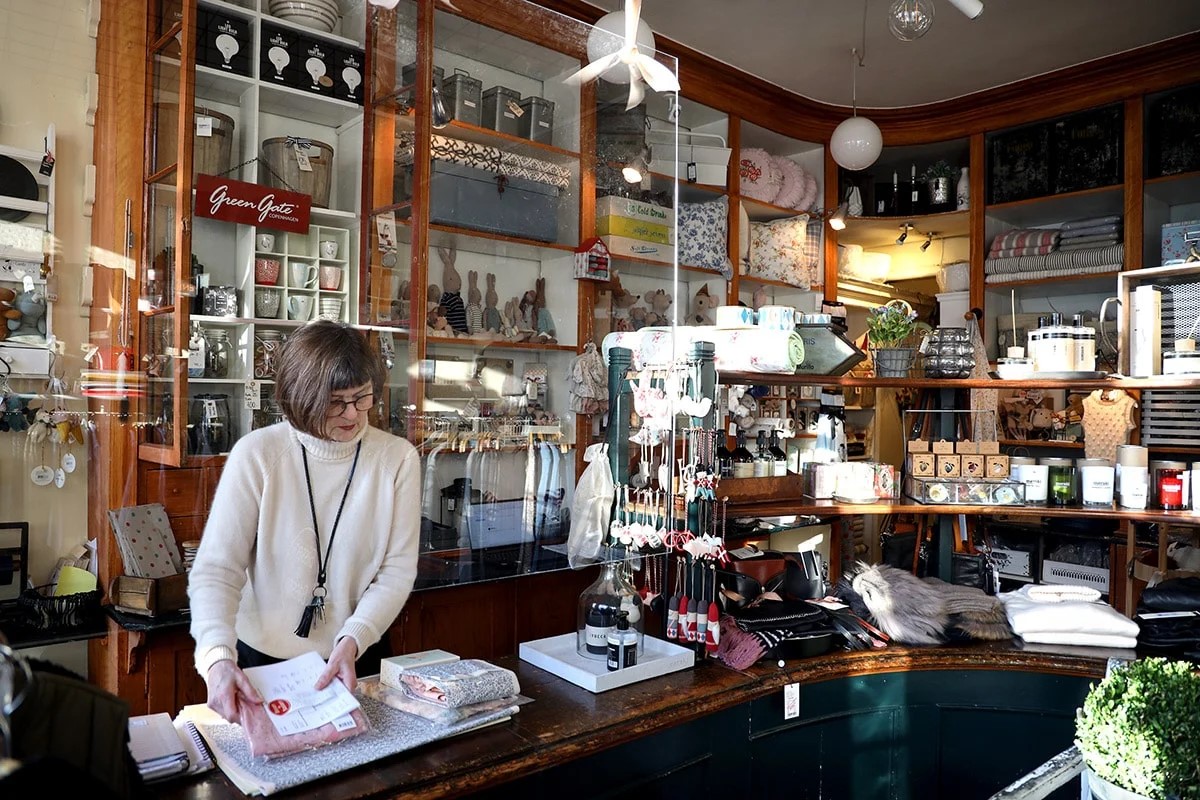 Kvinna packar varor bakom disken i en butik fylld med olika presentartiklar och inredningsdetaljer.