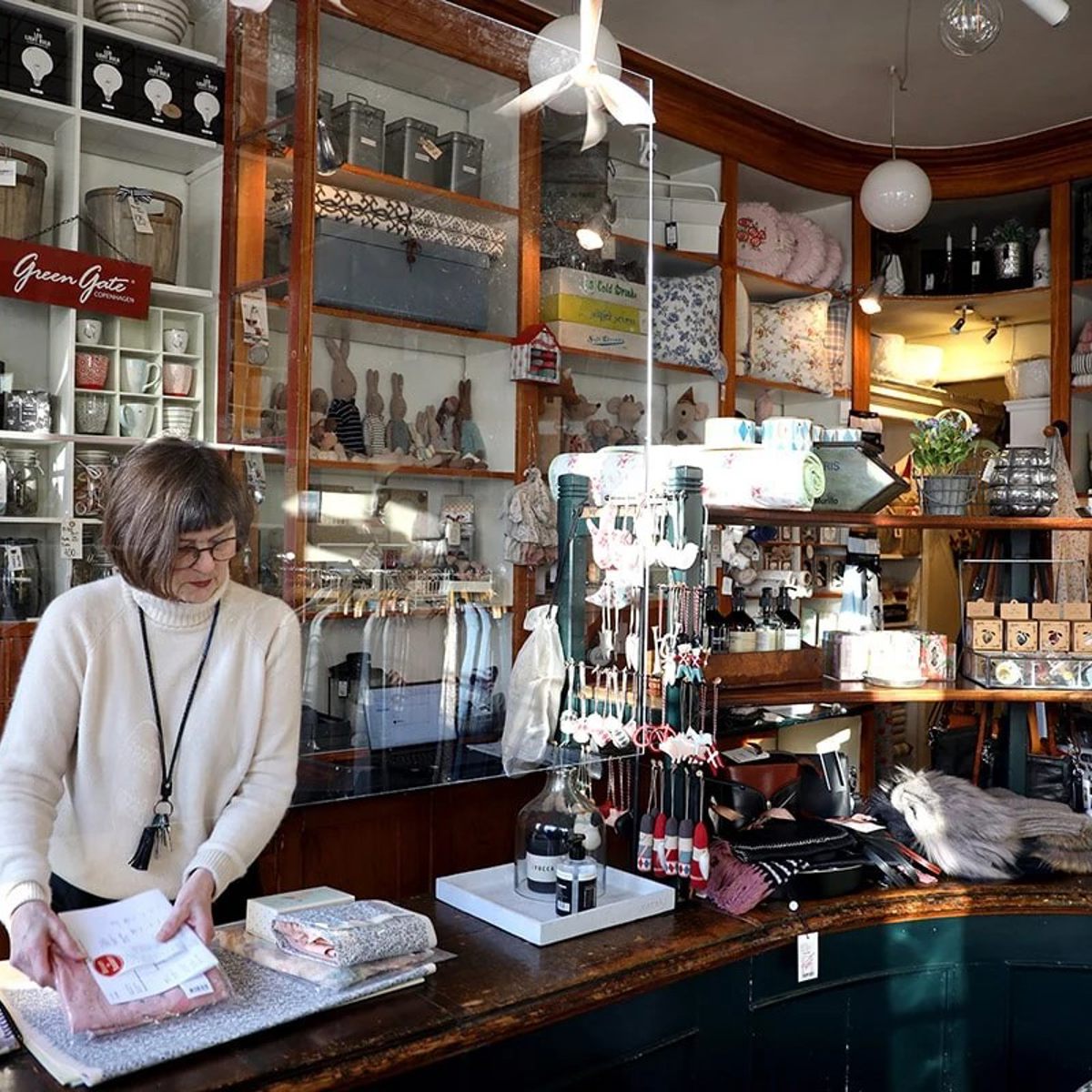 Kvinna packar varor bakom disken i en butik fylld med olika presentartiklar och inredningsdetaljer.