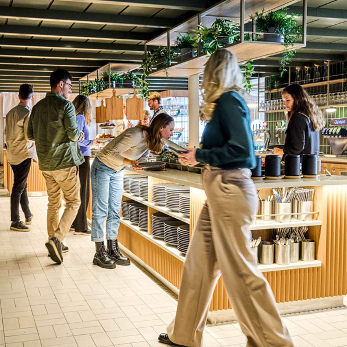 Cafégæster serverer sig selv ved en moderne buffet med planter og hyggelig atmosfære.
