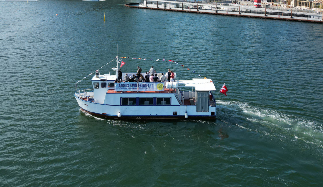 Aarhus Havn Rundfart båd sejler nær kajen med passagerer om bord i Aarhus Havn i fugleperspektiv.