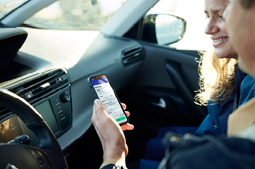 To personer i bil deler en smartphone, der viser en app på skærmen, tæt på bilens rat og instrumentbræt.