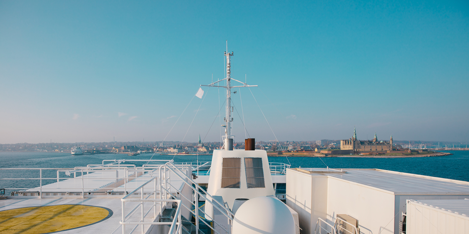 Dæk på færge med udsigt til Kronborg Slot og Helsingør fra havet under blå himmel.
