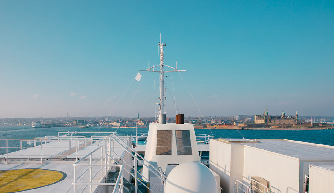 Dæk på færge med udsigt til Kronborg Slot og Helsingør fra havet under blå himmel.