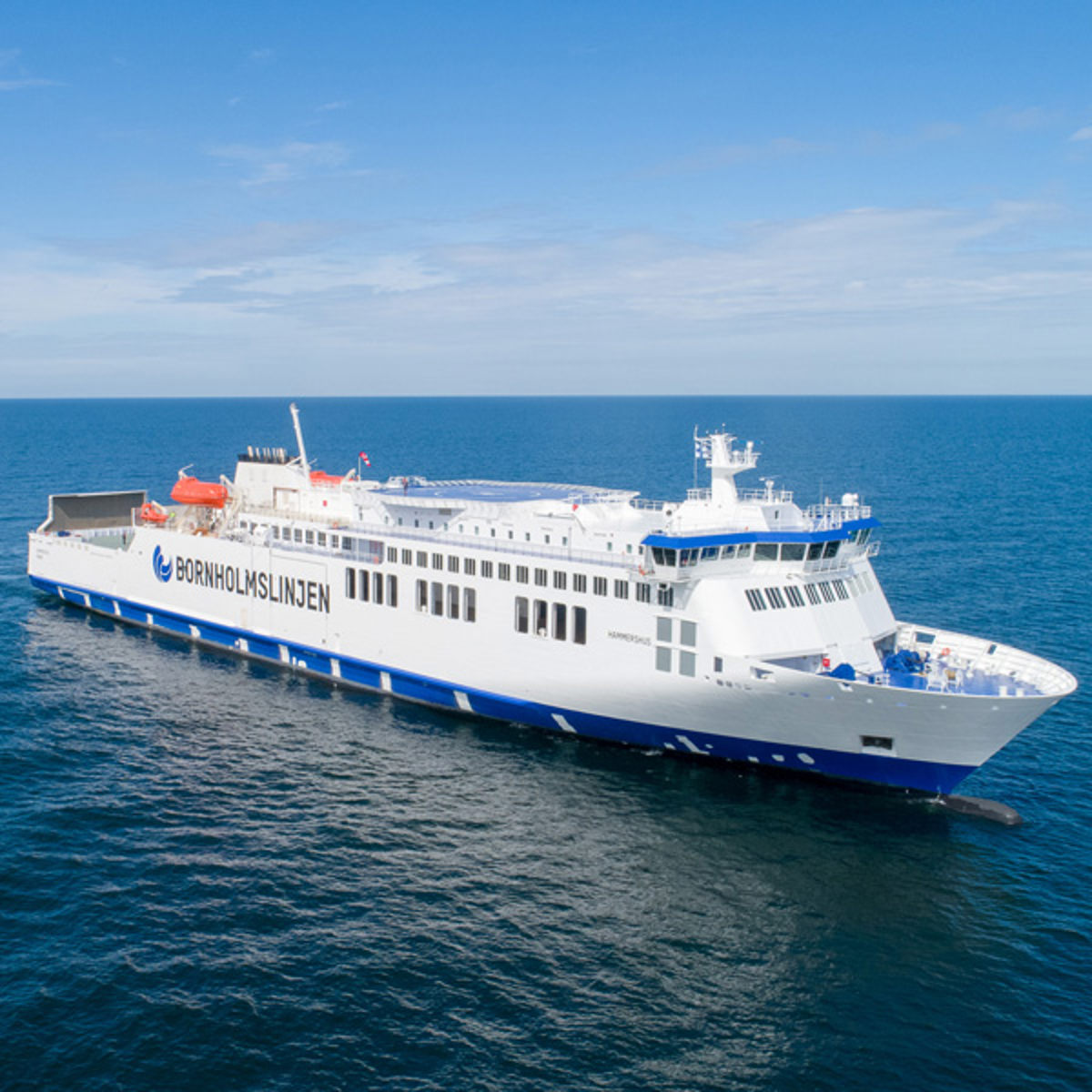 Bornholmslinjen ses fra venstre i fugleperspektiv omkranset af det blå hav og en lyseblå himmel.