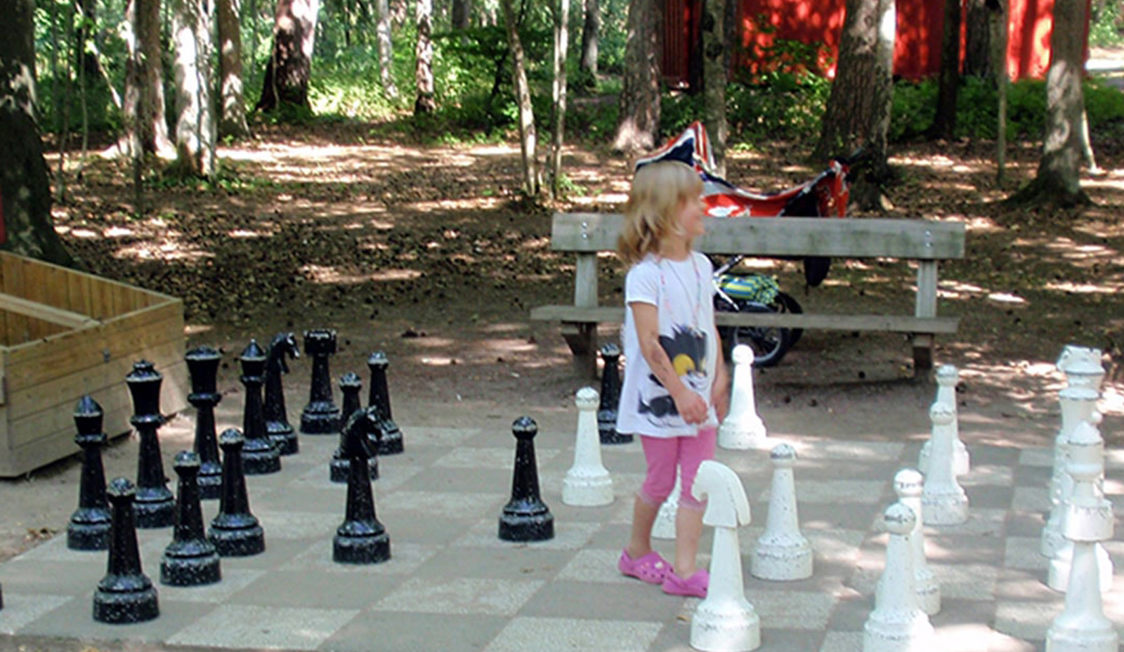 Lille pige spiller skak på et stort udendørs sort og hvidt skakbræt i skoven.