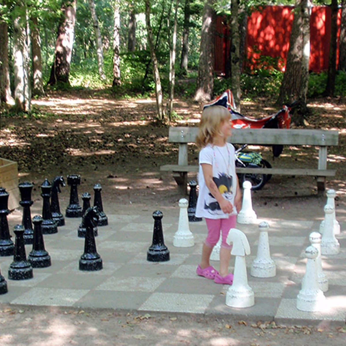 Lille pige spiller skak på et stort udendørs sort og hvidt skakbræt i skoven.