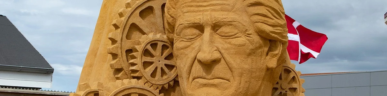Sandskulptur av ett ansikte med kugghjul på Hundested Sandskulpturfestival 22 i Danmark.