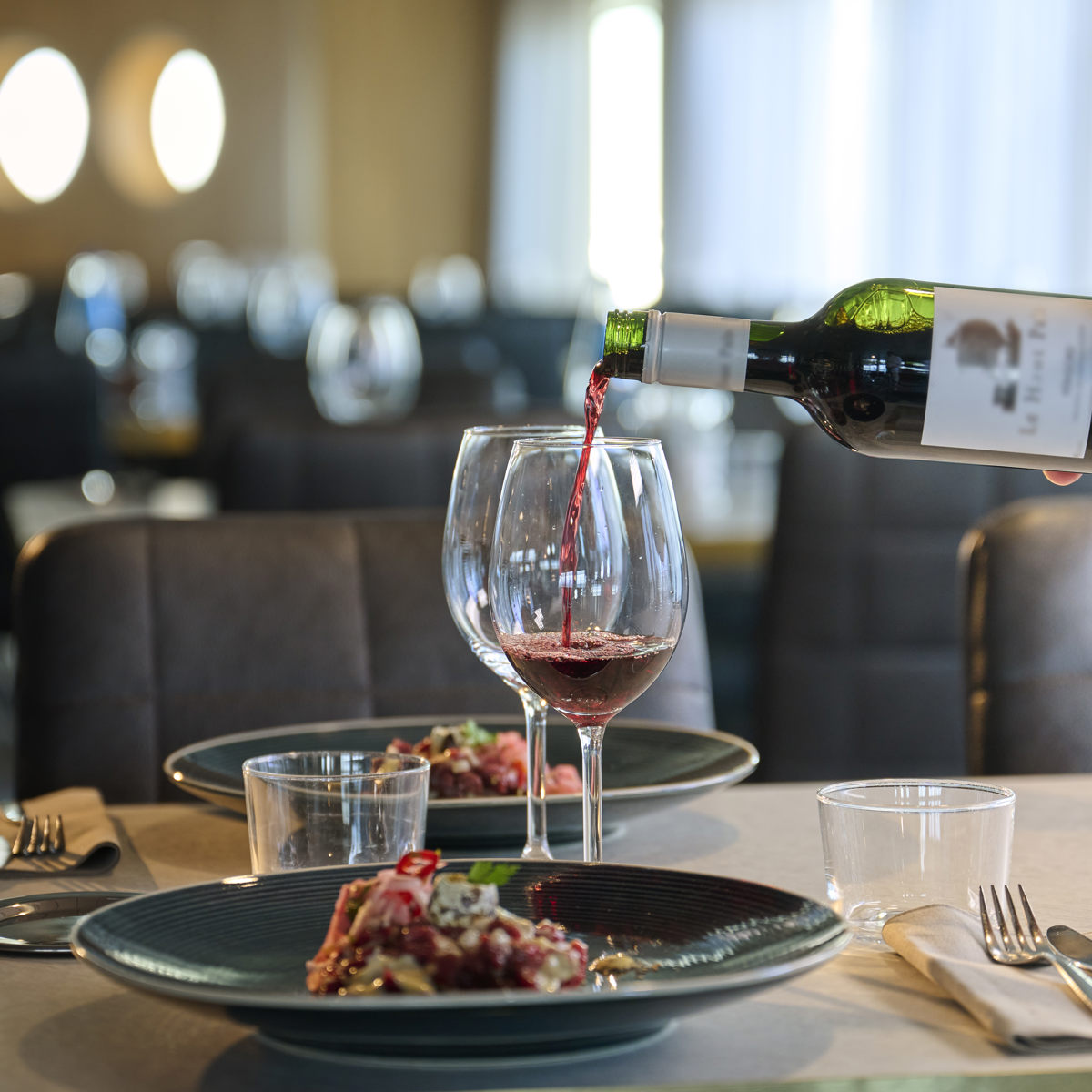 Rött vin hälls i ett vinglas vid ett dukat bord i en elegant restaurangmiljö.