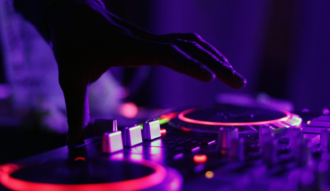 DJ:s hand justerar ljud på mixer i lila ljus under nattklubbskväll, närbild på DJ-utrustning.