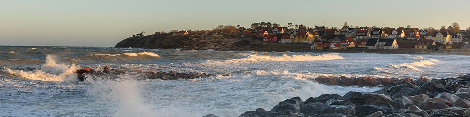 Vy över Hundested hamn och kust med vågor som bryter mot klippor i förgrunden.