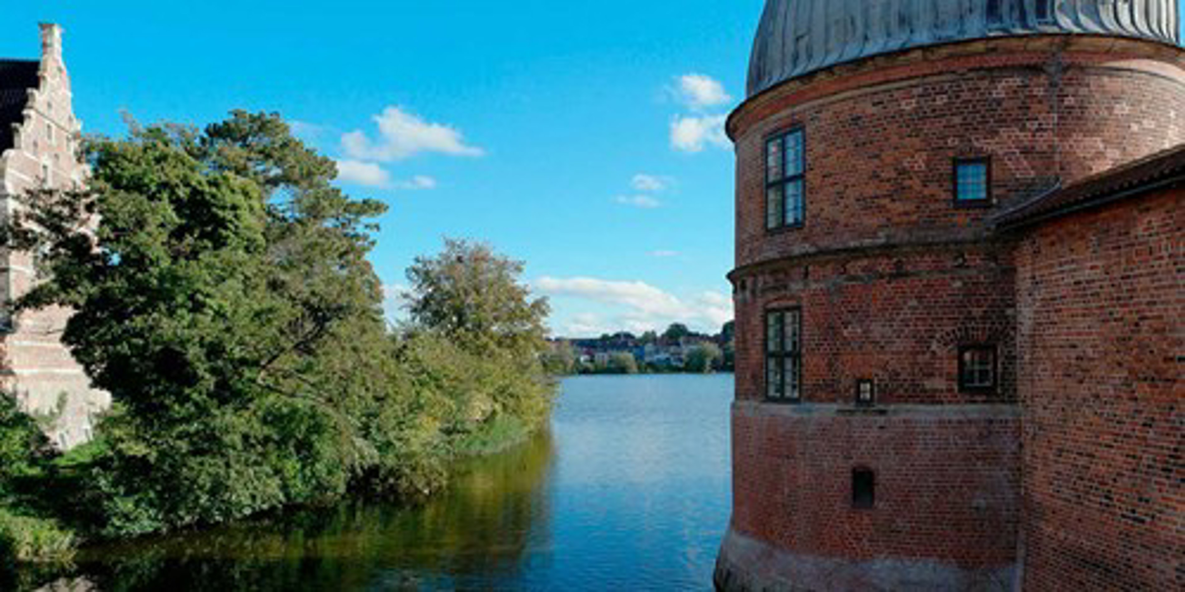 Rundt tårn af rødstensmur i renæssancestil ved søkant med blå himmel i baggrunden.