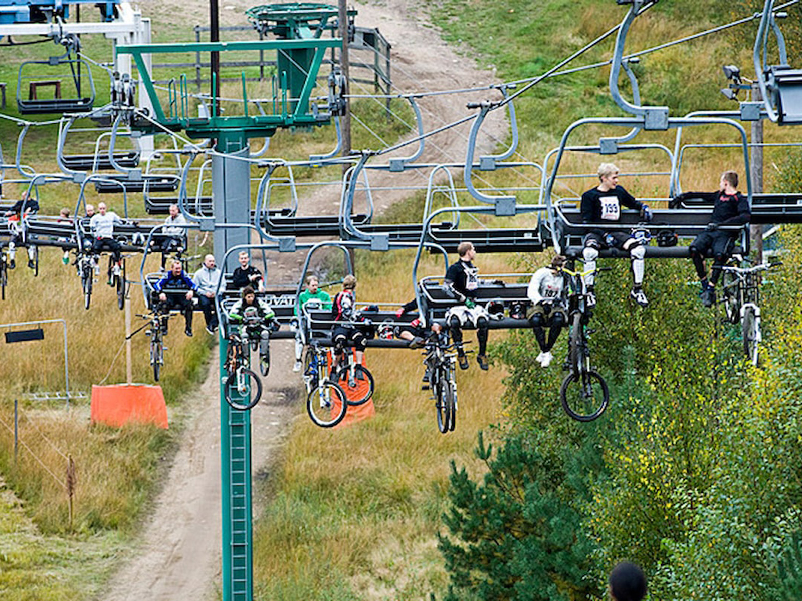 Cykelløbsdeltagere transporteres med stolelift ved bikepark i kuperet landskab med udsigt over grønne områder.