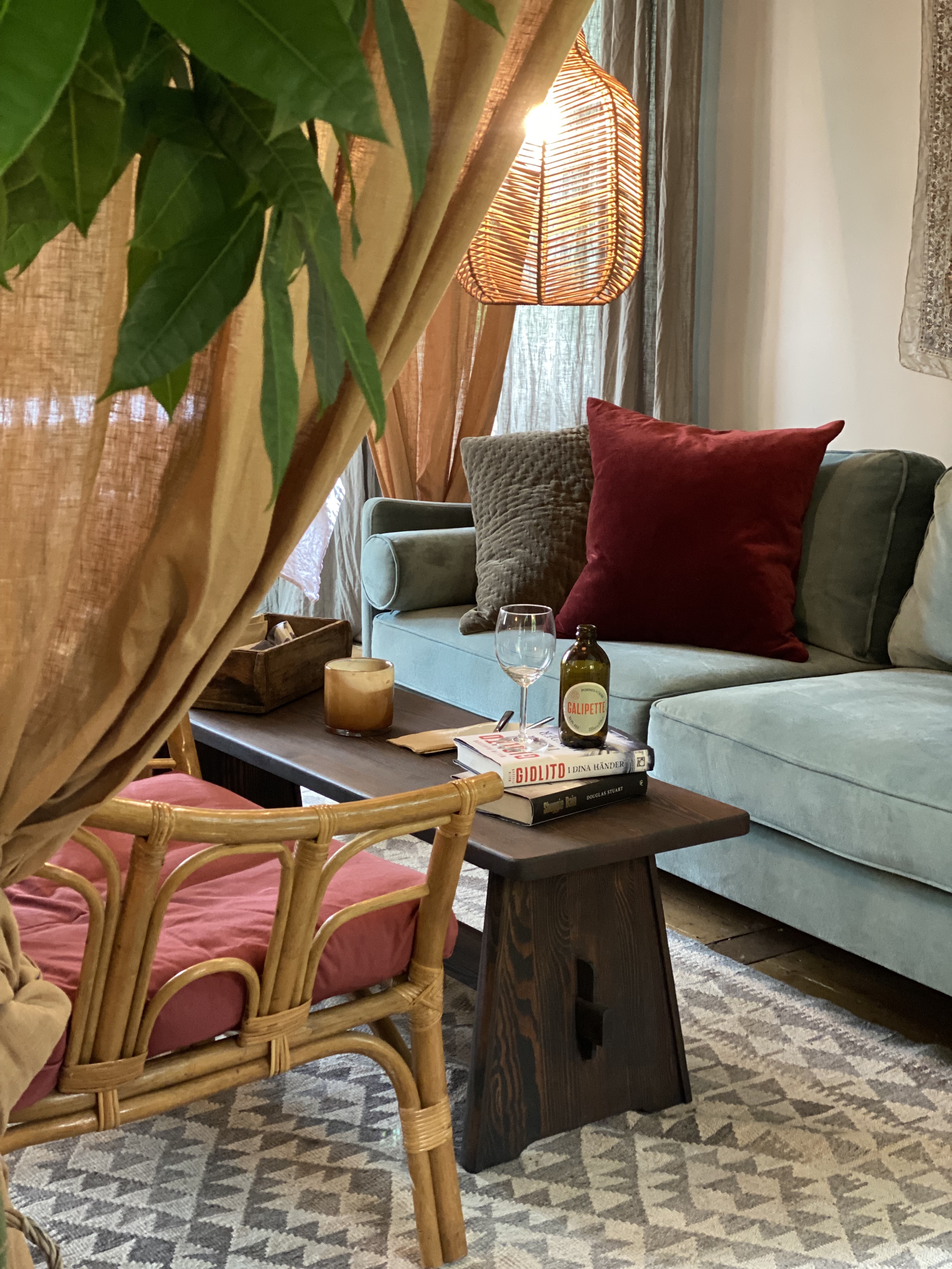 Hyggelig stue med en lyseblå sofa, mørkerød pude og lavt træbord med bøger og vinflasker på.