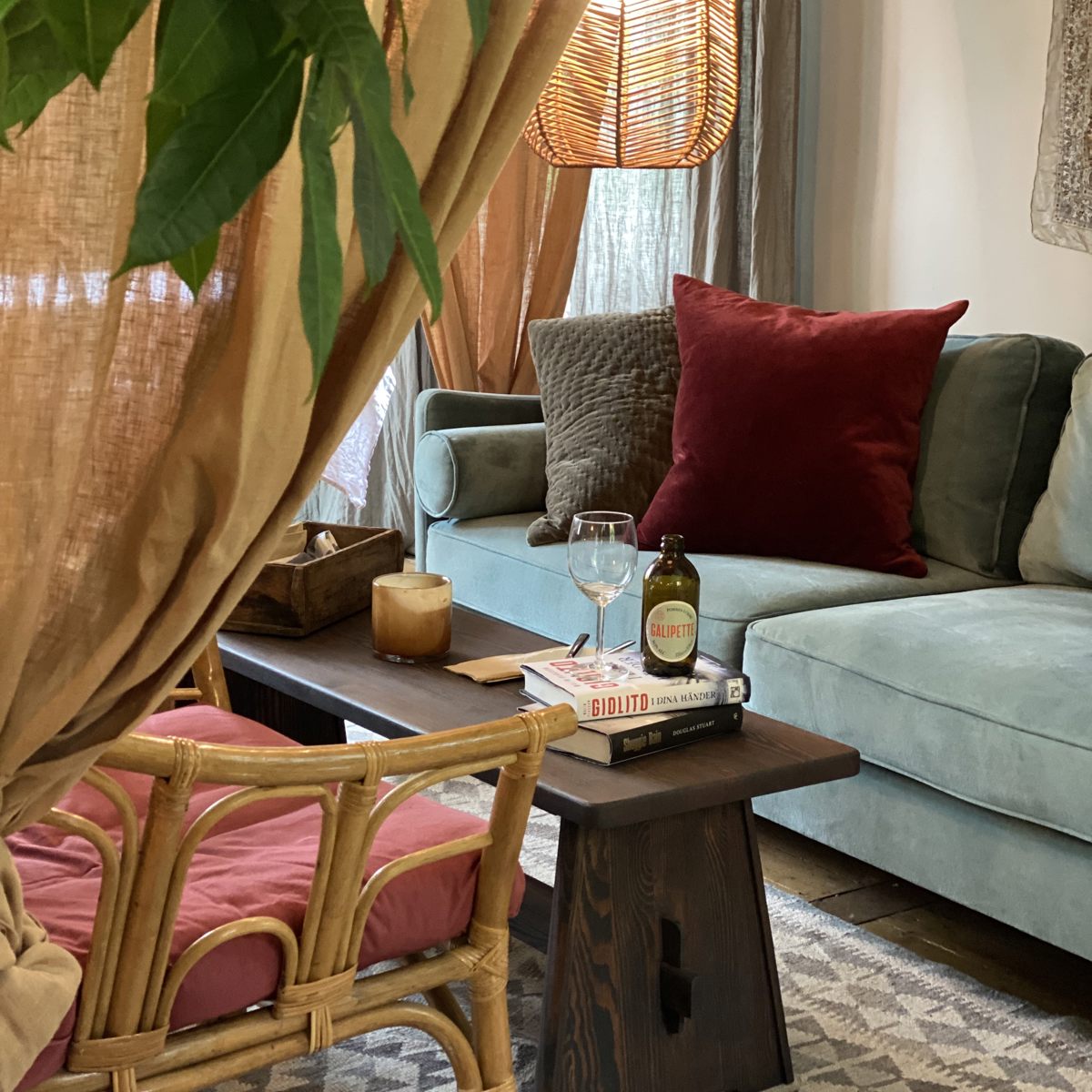 Hyggelig stue med en lyseblå sofa, mørkerød pude og lavt træbord med bøger og vinflasker på.