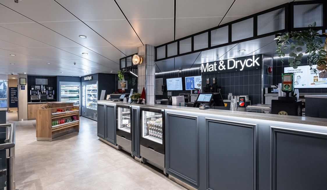 Servicedisk i modernt färjecafé "Mat & Dryck" med svart och silver inredning och framträdande menyskärmar.