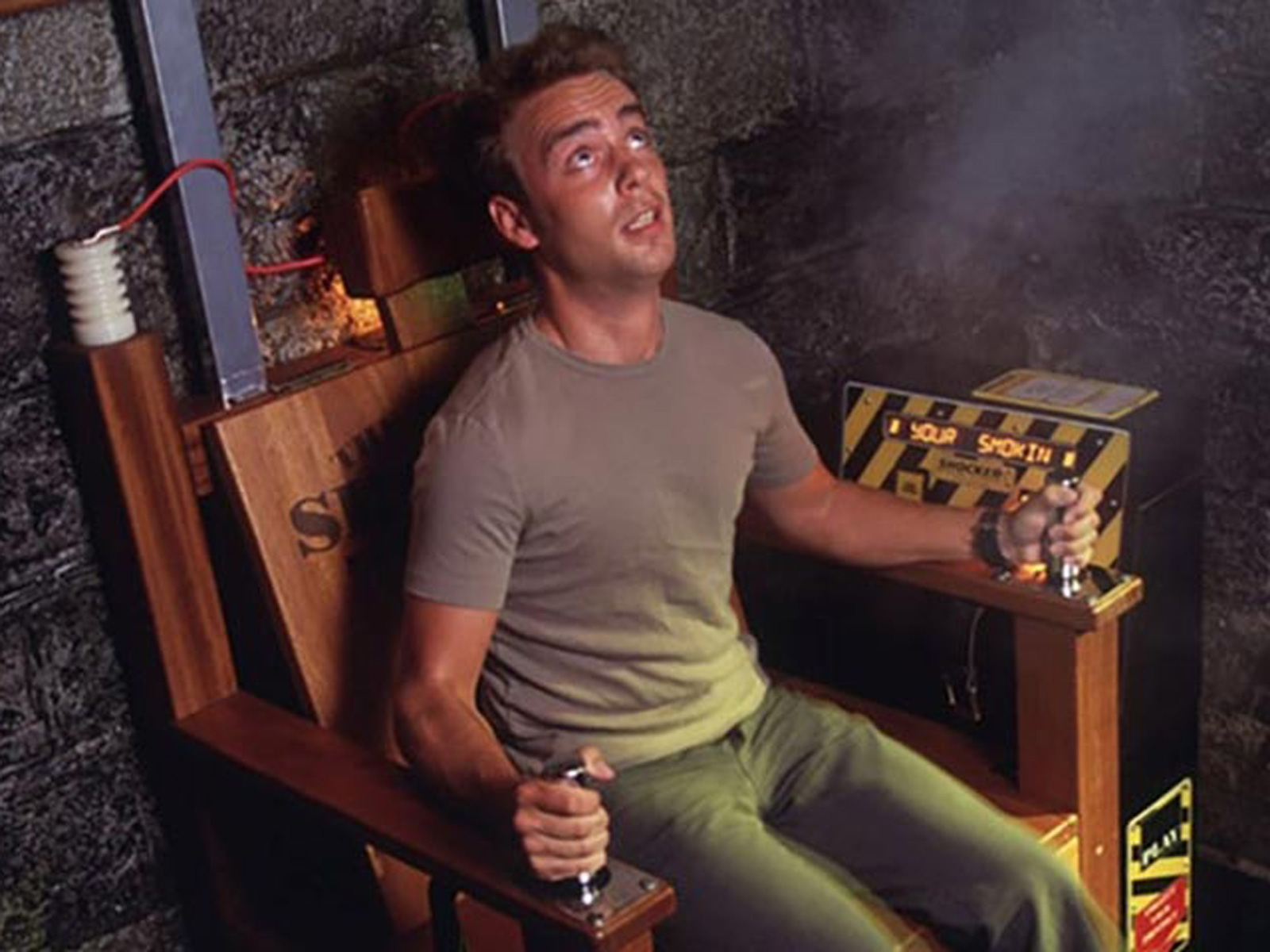 Person sitter i Mystic Exploratorie elektrisk stol med rök och ledningar i en stämningsfull inomhusmiljö.