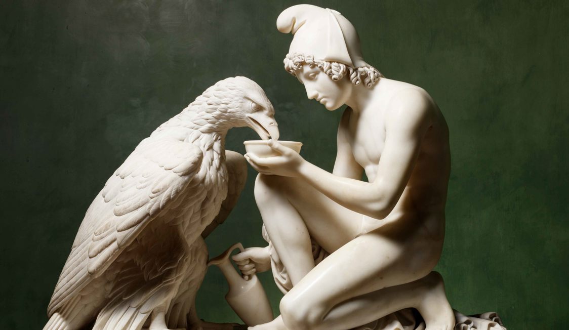 Statue af antik græsk mand og ørn, lavet af hvid marmor, fokuseret på det kunstneriske detaljer.