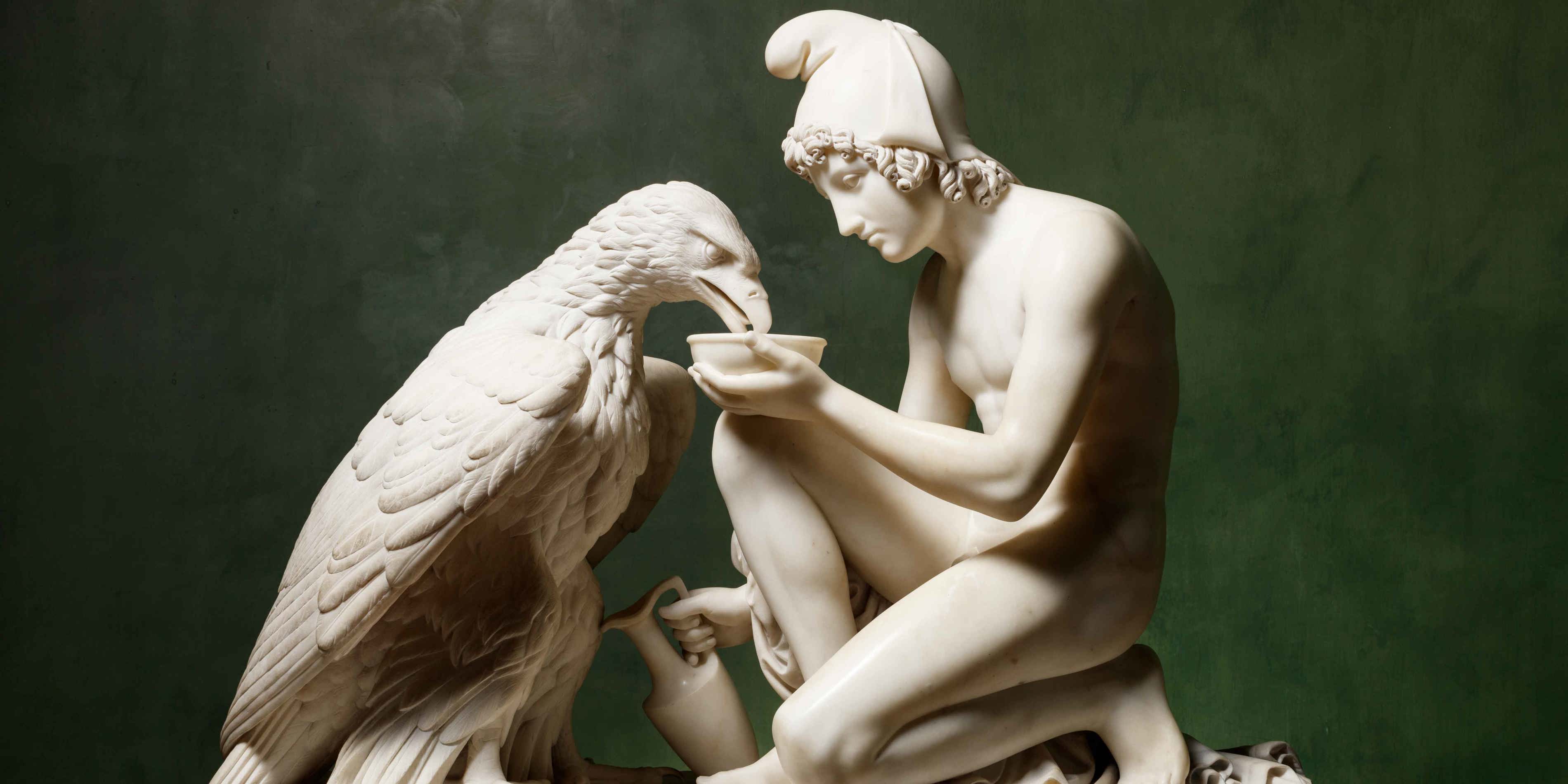 Statue af antik græsk mand og ørn, lavet af hvid marmor, fokuseret på det kunstneriske detaljer.