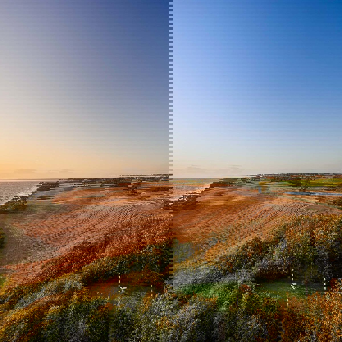 Solnedgangen ses over Samsøs marker med en hel klar og blå himmel.