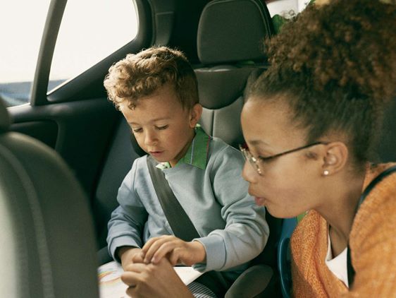 Barn og kvinde sidder sammen på bagsædet af bil, barnet fokuseret på at lege med legetøj i rolig atmosfære.