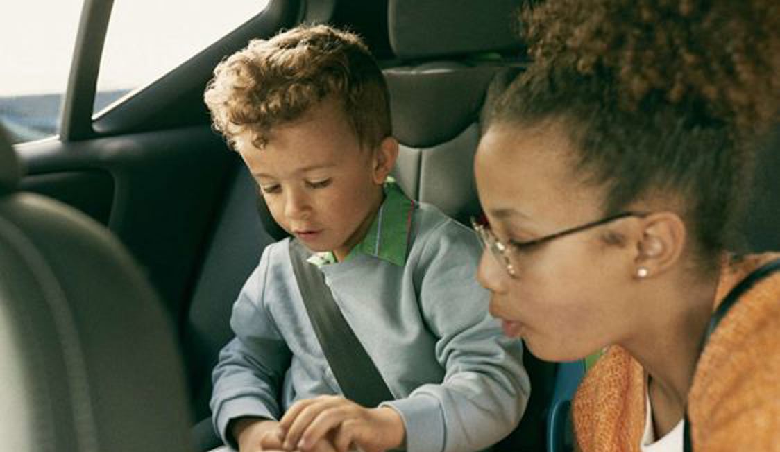 Barn og kvinde sidder sammen på bagsædet af bil, barnet fokuseret på at lege med legetøj i rolig atmosfære.