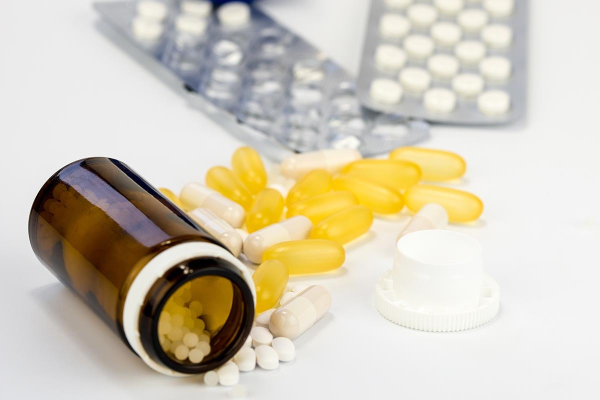 Öppet pilleglas med gula och vita piller på ett vitt bord, fokus på huvudämnet.