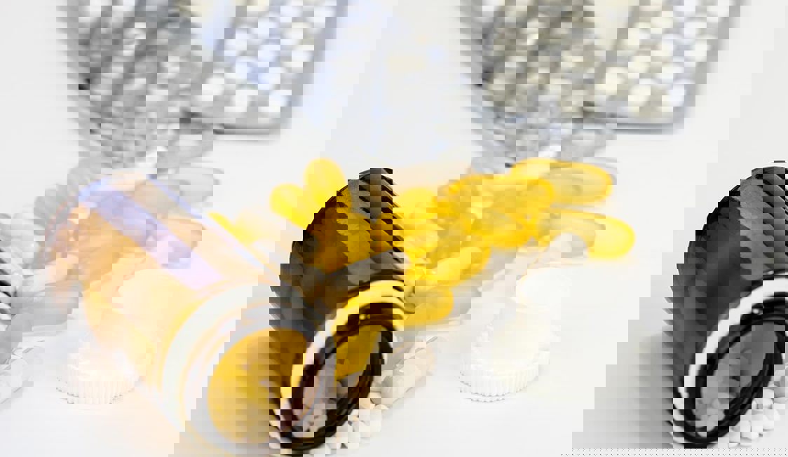 Öppet pilleglas med gula och vita piller på ett vitt bord, fokus på huvudämnet.