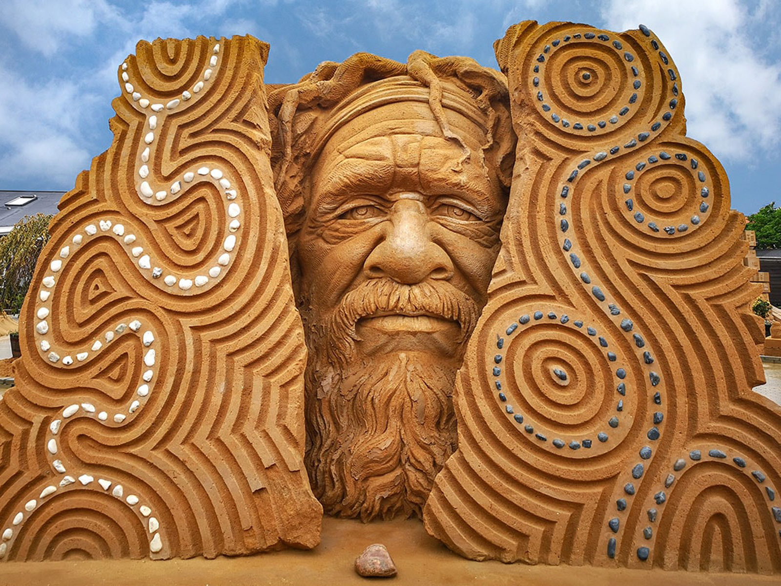 Storskalig sandksulptur av en gammal mans ansikte i Hundested, med detaljerade mönster och stenar.