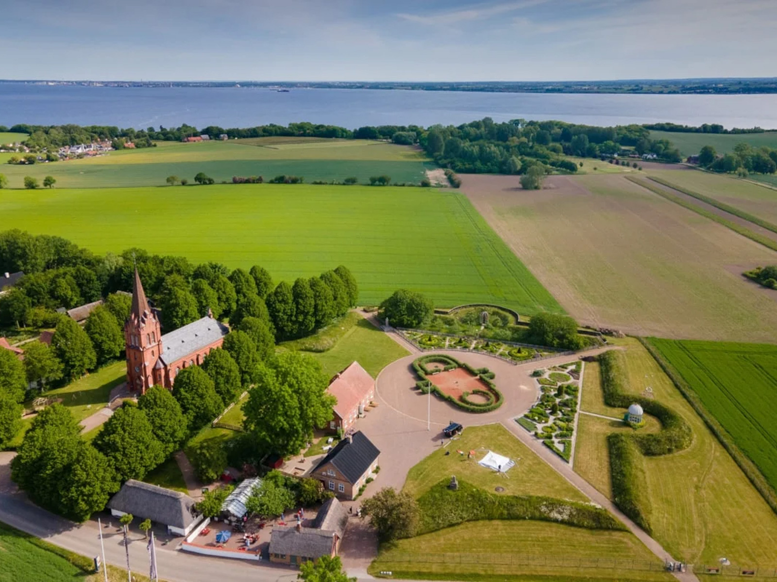 Sankt Jørgens Kirke omgivet af grønne marker set fra fugleperspektiv nær sø i landskabet.