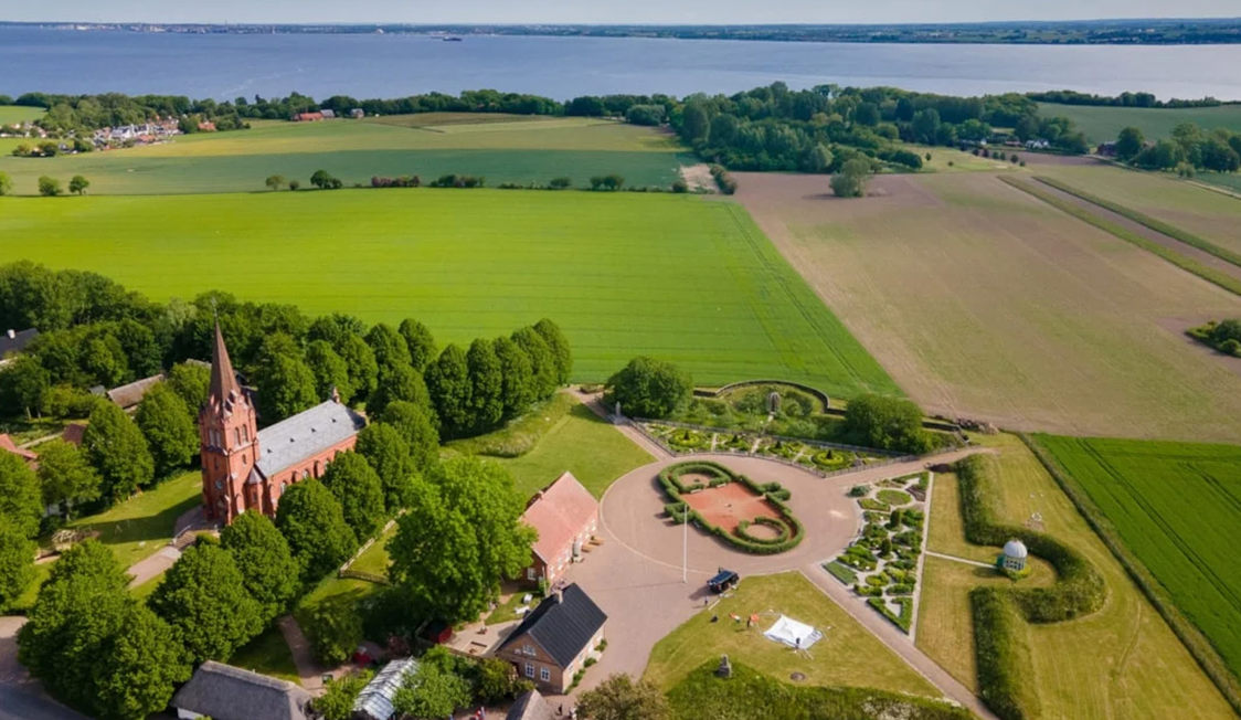 Sankt Jørgens Kirke omgivet af grønne marker set fra fugleperspektiv nær sø i landskabet.
