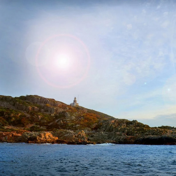 Fyrtårn på en klippe med den klare himmel og solens stråler over landskabet i horisonten.