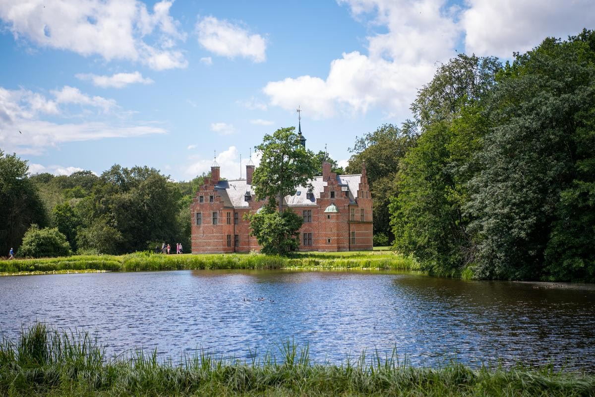 Hillerød slot speglas i sjön med en vacker vy under blå himmel.