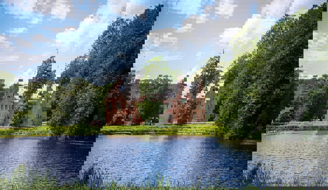 Hillerød slot speglas i sjön med en vacker vy under blå himmel.