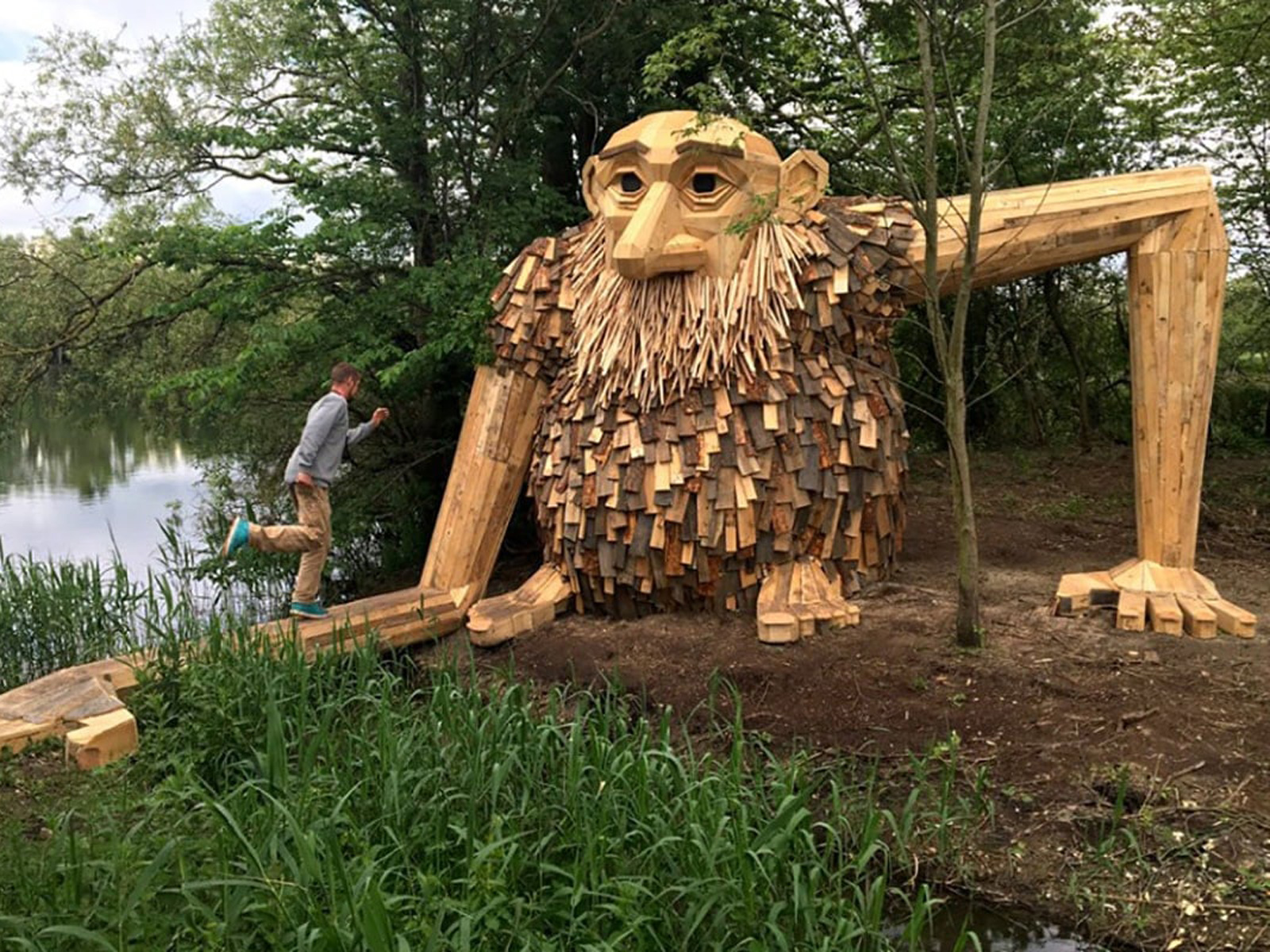 Jättestor träskulptur av troll i skogen, Kph Jättetrollen Teddy, med man som klättrar på dess arm.