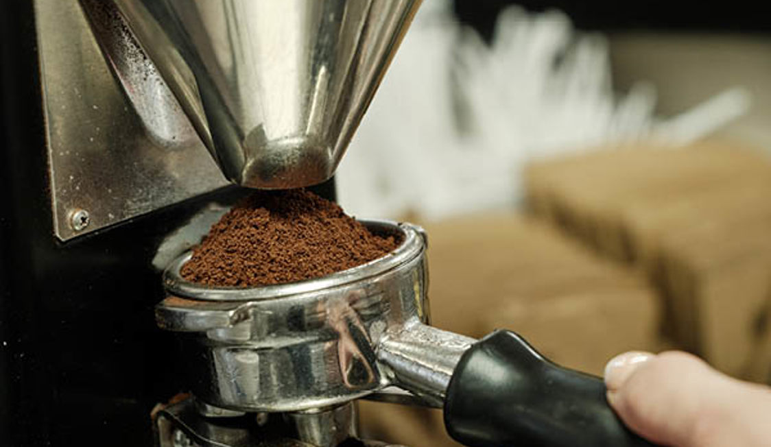 Kaffeemühle mahlt frische Kaffeebohnen in einen Siebträgerhalter für Espresso.