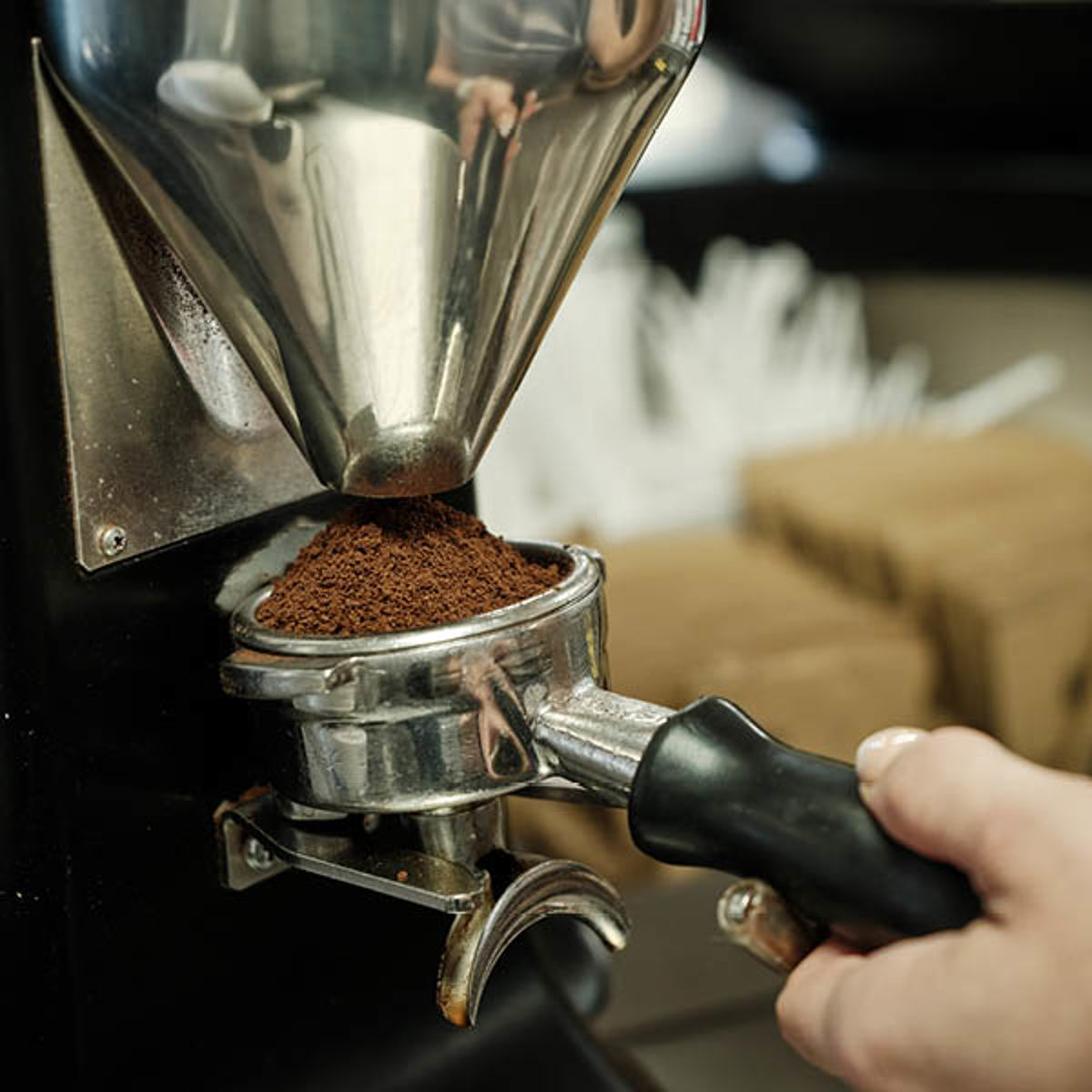Kaffemølle maler friske kaffebønner ned i en portafilterholder, klar til at brygge espresso.