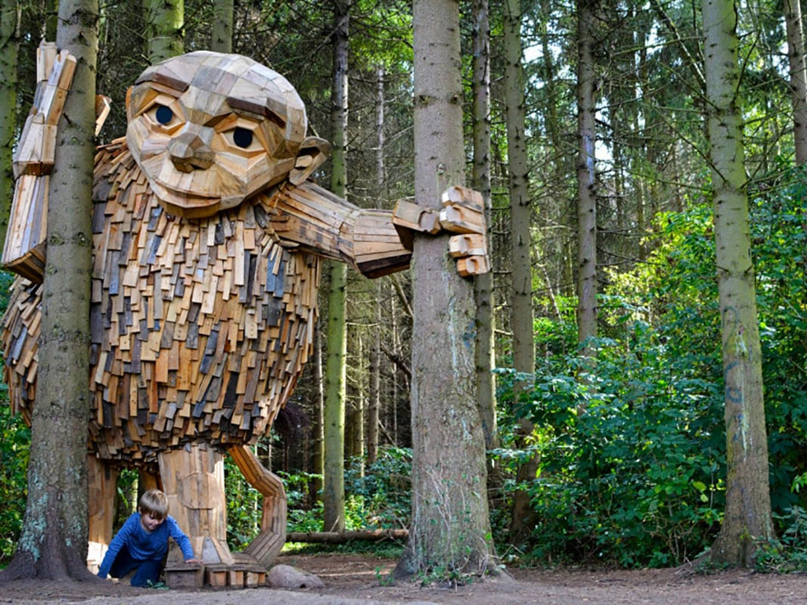 Stor träskulptur av trollet Tilde omgiven av träd i skogen.