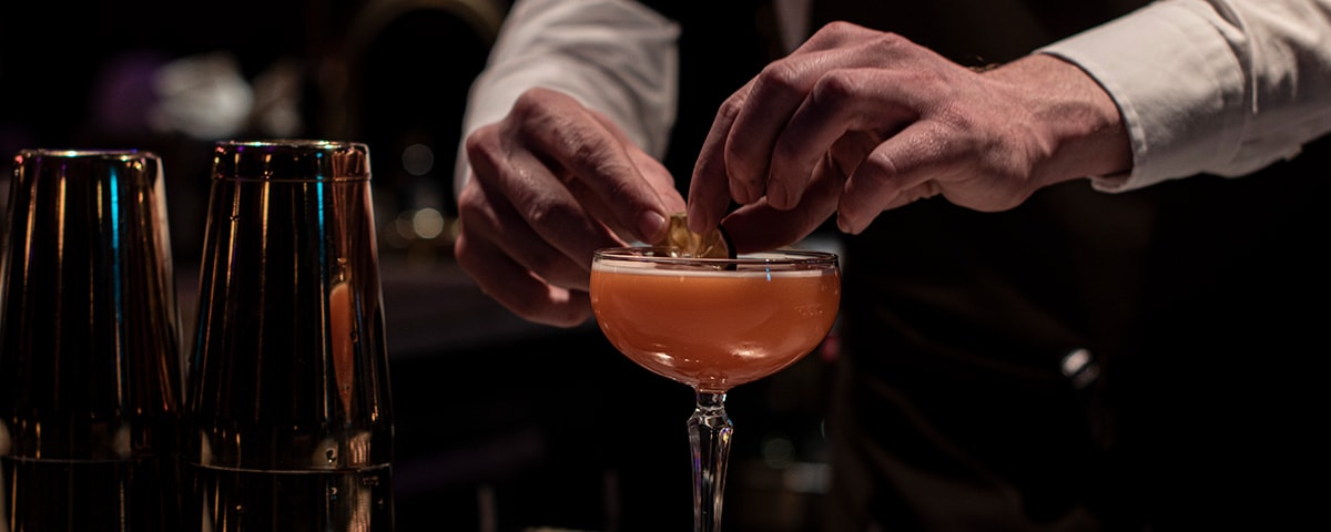 En bartender er ved at færdiggøre en drink med garnish.