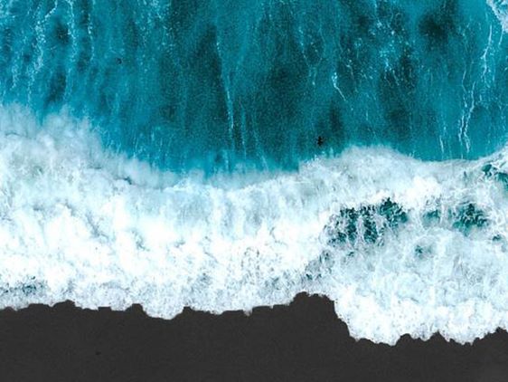 Bølger bryder mod kysten set fra oven med turkisblåt hav og skummende hvidt vand.