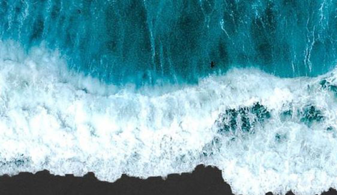 Bølger bryder mod kysten set fra oven med turkisblåt hav og skummende hvidt vand.