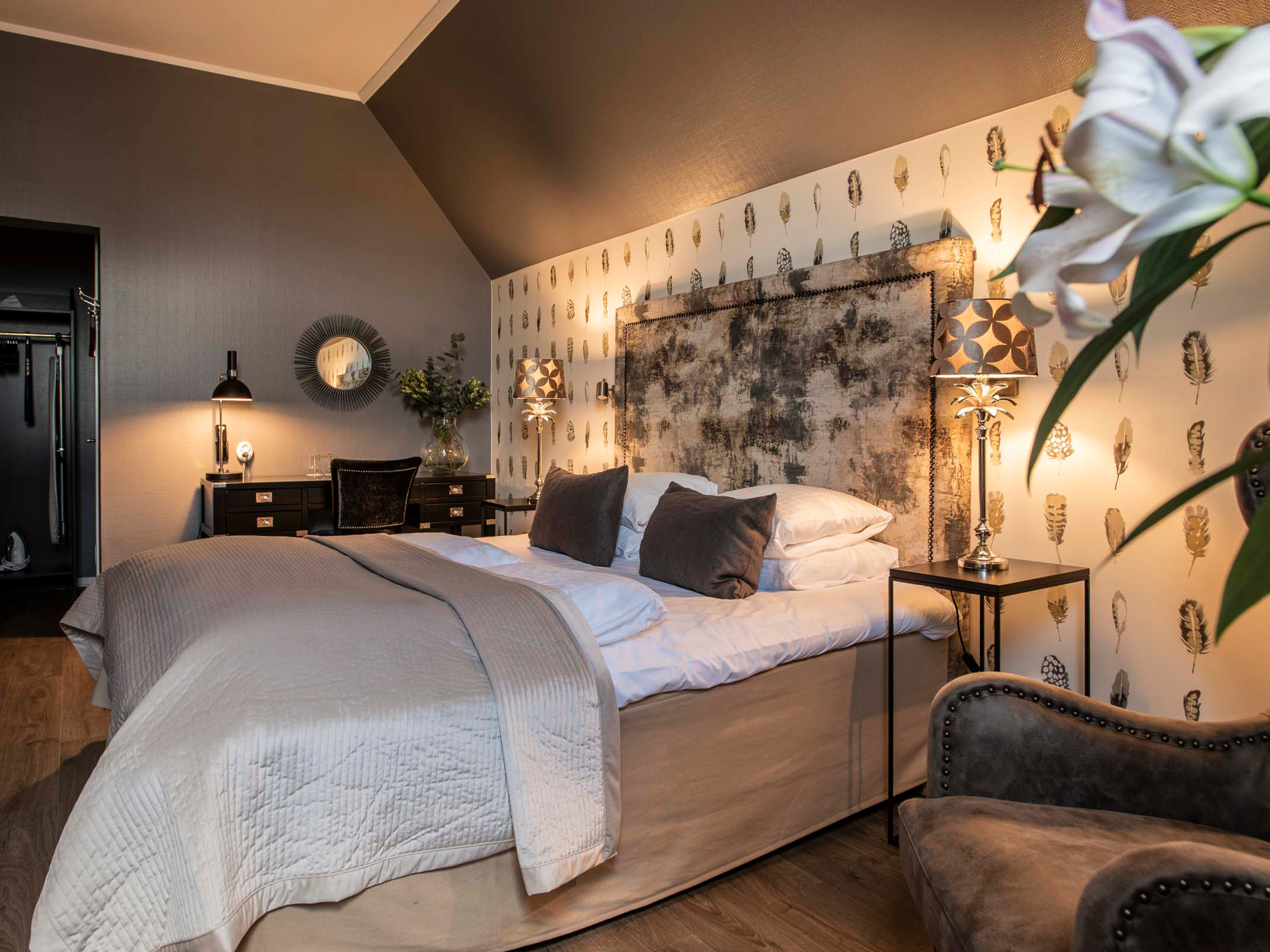 Elegance soveværelse med stor seng, polstrede puder og moderne dekorationer i varme nuancer.