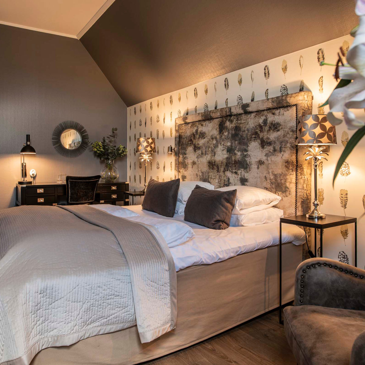 Elegance soveværelse med stor seng, polstrede puder og moderne dekorationer i varme nuancer.
