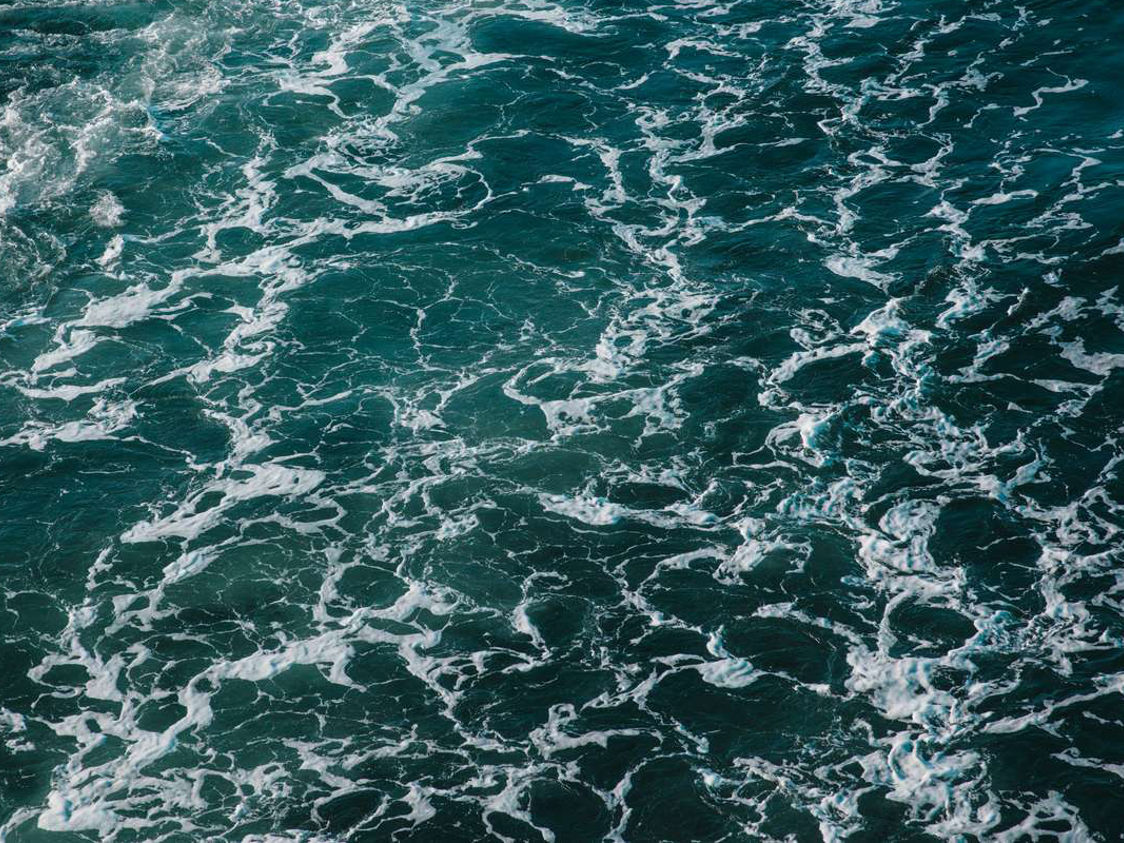 Havets vågor med skumspår sett ovanifrån, ger en dramatisk bild av det vidsträckta öppna havet.