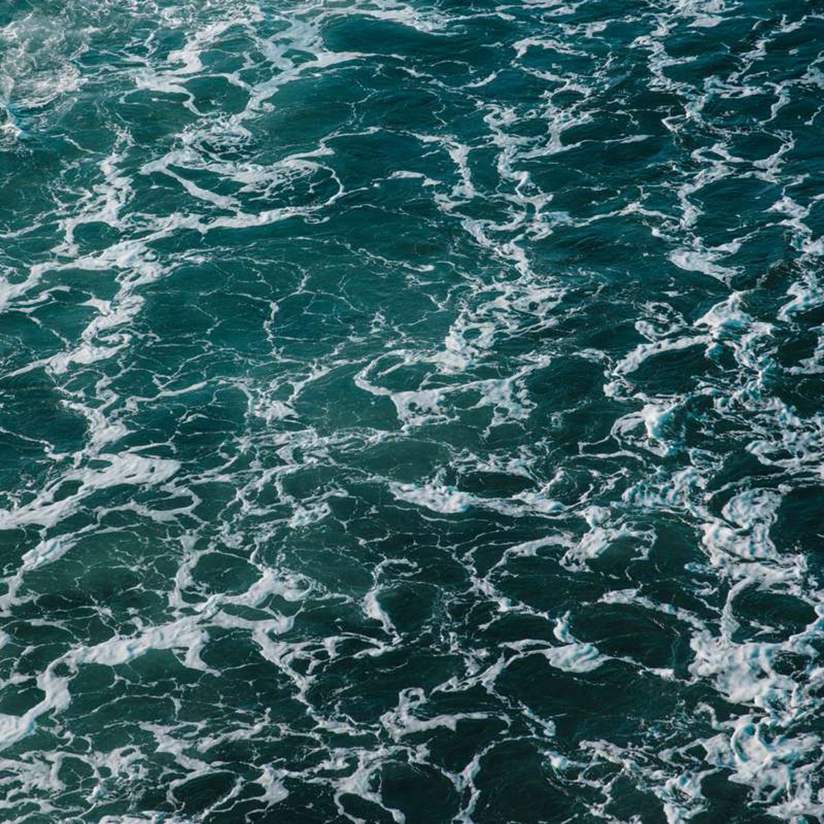 Havets bølger med spor af skum set i fugleperspektiv, giver et dramatisk billede af det åbne hav.