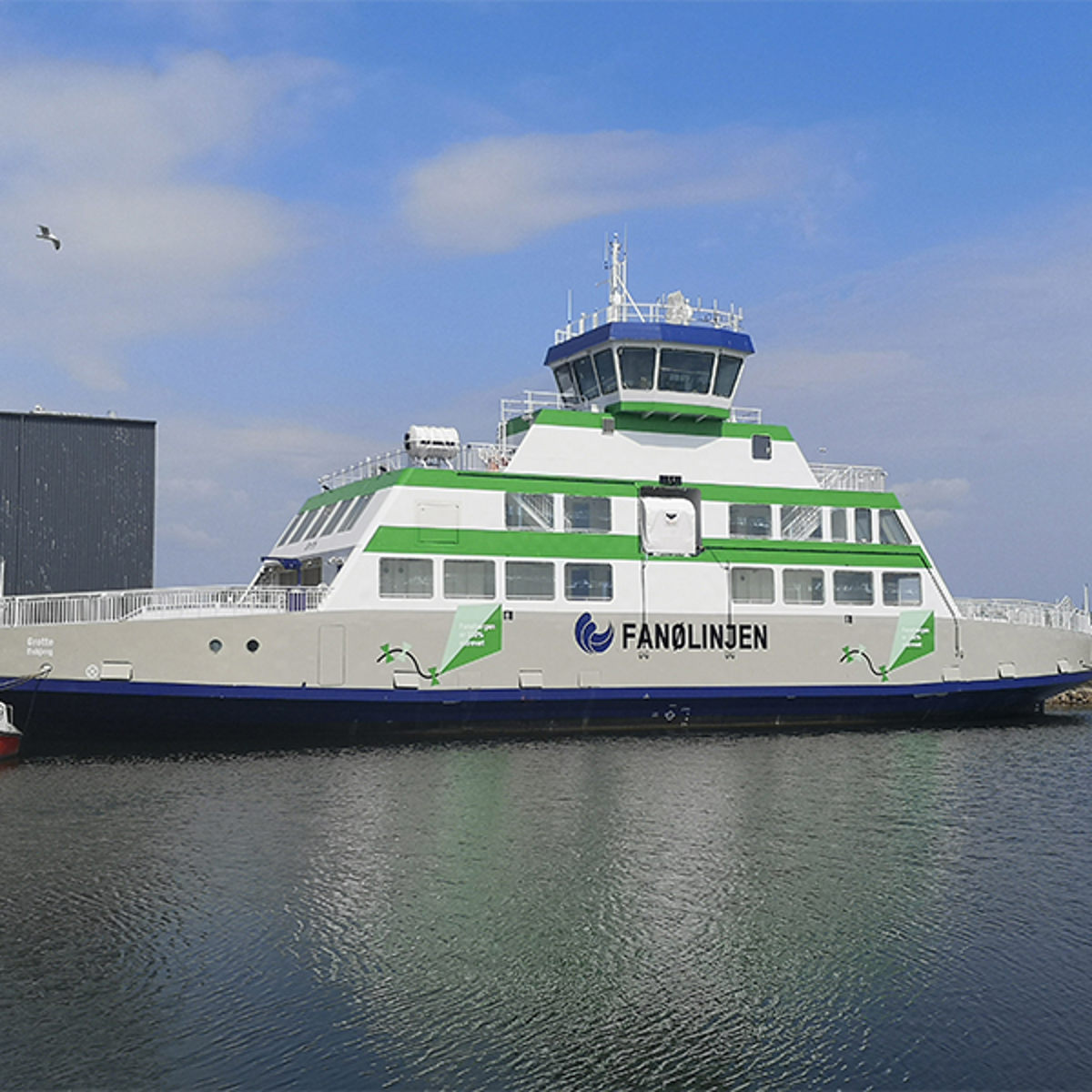 Fanølinjen færge ved kaj i havnemiljø med blå himmel og spejlblankt vand.