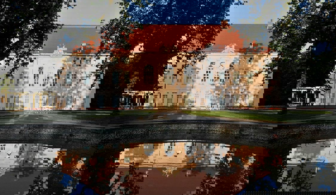 Berlin Schönhausen sett från framsidan med spegelblankt vatten och kvällssol.