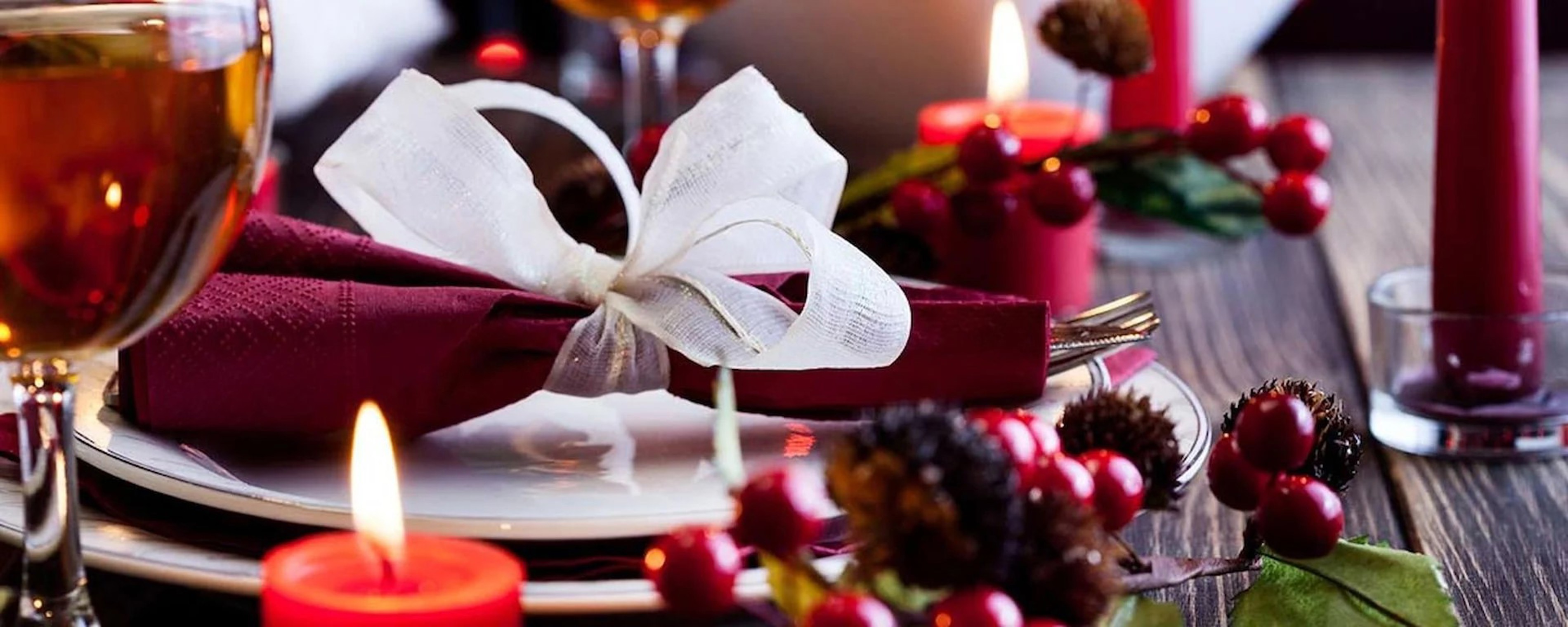 Elegant julebord med röd servett och vit rosett vid stearinljus och glögg i festlig miljö.