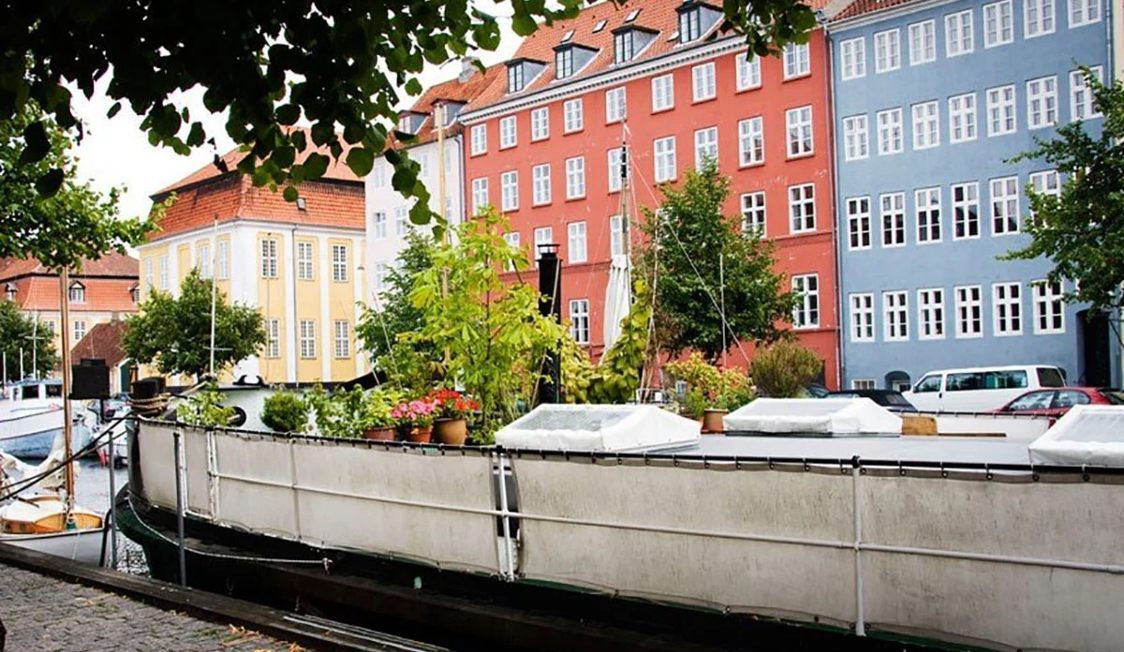 Kristianshavn husbåt vid färgglada byggnader och kanaler i Köpenhamn med gröna växter ombord.