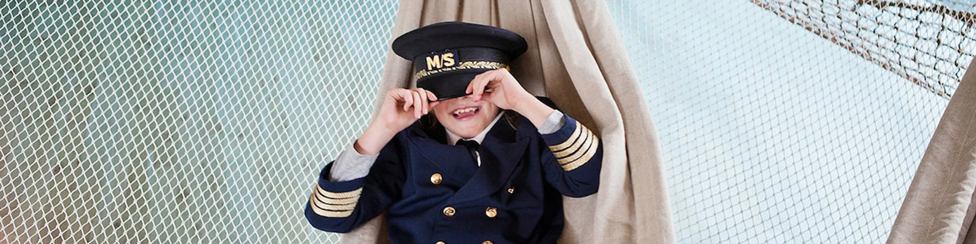 Pojke i sjömanskostym med kaptensmössa leker på Museet For Sjöfart, ler under nätet ombord på en båt.