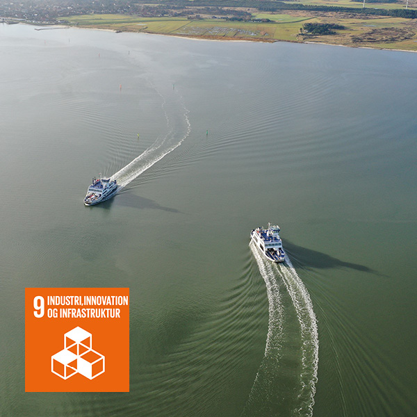 To færger sejler side om side på roligt vand set fra fugleperspektiv.